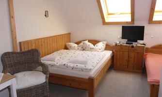 A cozy bedroom with wooden furniture and a double bed. There is a window with plenty of light and a television.