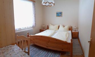 A cozy bedroom with a large bed and bright pillows. The room has a wood look and a window with plenty of natural light.