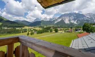 A picturesque view from a balcony over green meadows and majestic mountains. The sky is partly cloudy and radiates fresh, alpine air.