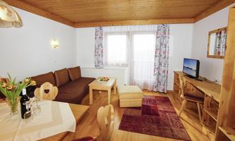 A cozy living room with a wooden ceiling and friendly light. There is a dining area, a seating area, and a television.