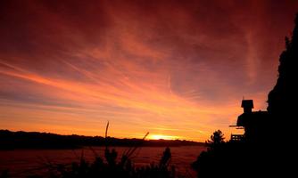 A stunning sunset with colorful clouds in the sky. Silhouettes of a building and trees at the edge of the picture.