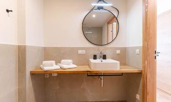 A modern bathroom with an elegant sink and a large round mirror. Towels are neatly arranged on a wooden shelf.