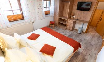 A cozy bedroom with a large bed and red pillows. The warm wooden furniture and the window create an inviting atmosphere.