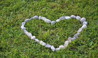 A heart made of stones lies on green grass. The natural arrangement of the stones creates a loving atmosphere.
