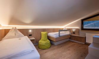 A modern room with two single beds and a comfortable bean bag in bright green. The room is well-lit and features a pleasant wooden decor.