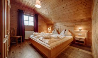 A cozy wooden bedroom with a double bed and soft pillows. Large windows let in plenty of daylight.