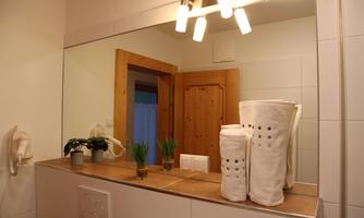 A modern bathroom with a large mirror and warm lighting. Clean towels and small plants are on the sink.