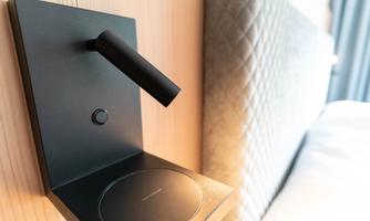 A modern desk lamp on a wall with wooden paneling. Next to it is a round switch.
