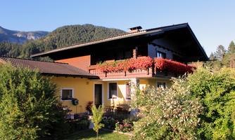 A beautiful house with colorful flower balconies and a well-kept garden. In the background, mountains and a clear sky are visible.