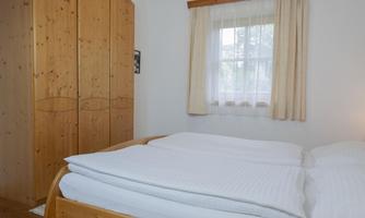 A bright bedroom with a large double bed and a wooden wardrobe. The window lets in plenty of daylight and creates an inviting atmosphere.