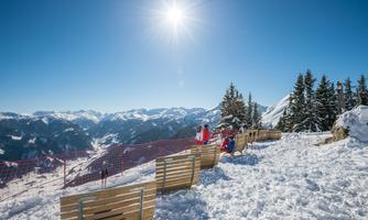 A snow-covered mountain with a clear blue sky view. People are sitting on wooden loungers and enjoying the scenery.