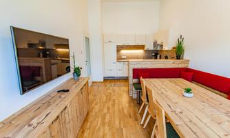A modern kitchen with a large wooden dining table and red benches. The walls are light and create a friendly atmosphere.