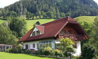 A cozy house with a red roof in a green landscape. In the background, gentle hills and trees can be seen.