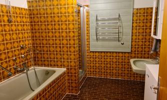A bathroom with orange tiles and a bathtub. There is a shower, a small sink, and a towel rack.