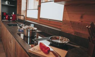 A modern kitchen with wooden paneling and large windows. On the countertop, cooking pots and a red pepper on a cutting board can be seen.