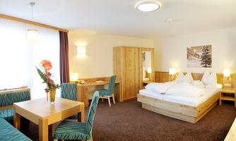 A cozy hotel room with a double bed and a table with chairs. The decor is modern and wood-paneled, with plenty of natural light.