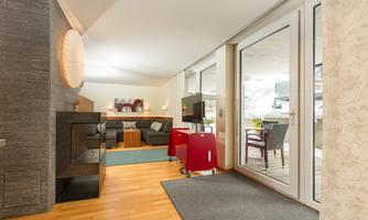 A modern living room with a cozy couch and a fireplace. Large windows provide a view outside and ensure plenty of daylight.
