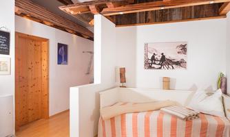 A cozy bedroom with a daybed and a wood stove. The walls are painted in warm colors, and a picture of landscapes creates a pleasant atmosphere.