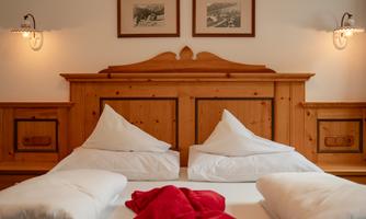 A cozy bedroom with wood decor and two beds. On the bed lies a red blanket and the walls are adorned with pictures.