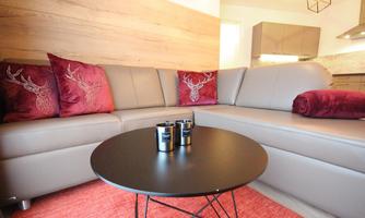 A modern living room with a large beige sofa and burgundy cushions. In the center is a round black table on a carpet.