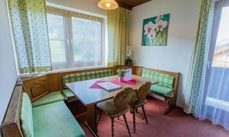 A cozy dining area with a corner and a table. The walls are light and adorned with a floral painting.