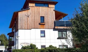 A modern apartment building with wood cladding and a large window front. The clear blue sky highlights the amenities of the accommodation.