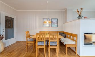A cozy dining area with wooden furniture and a harmonious decor. The walls are light, and there are decorative pictures and plants.