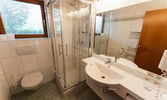 A modern bathroom with a shower and a sink. There are windows that let in daylight and bright tiles.