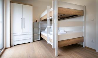 A modern bedroom with a bunk bed and a white wardrobe. The room has light wooden floors and large windows that provide plenty of light.