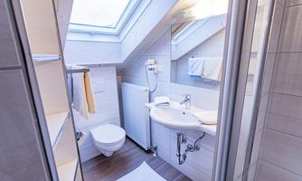 A modern bathroom with a skylight and bright furnishings. It features a shower, sink, and a toilet.