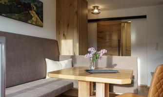 A modern dining room with a wooden table and a bench. There is a vase with flowers on the table and stylish lighting.