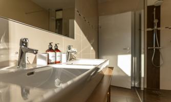 A modern bathroom with an elegant sink and two sink faucets. The space is bright and friendly, with a shower in the background.