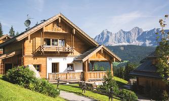 A cozy wooden house surrounded by nature and gentle hills. In the background, majestic mountains can be seen.