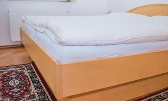A comfortable bed with a white bedspread in a bright bedroom. The floor is made of wood and there is a rug beside the bed.