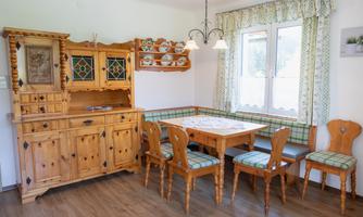 A cozy dining area with a wooden table and chairs. In the background, there is a rustic sideboard and the window lets in plenty of light.