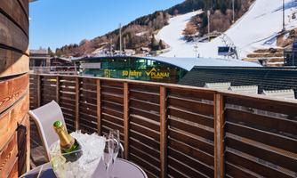 A balcony with a view of snow-covered mountains. In the middle stands a champagne glass and an ice cooler.