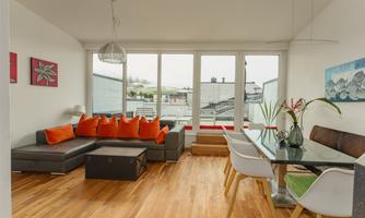 A modern living room with a comfortable sofa and a dining table. Large windows offer a view of the surroundings.