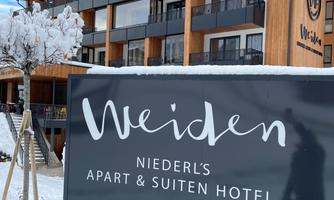 An apart-hotel named Weiden, surrounded by snow. The entrance is modern in design and offers an inviting atmosphere.