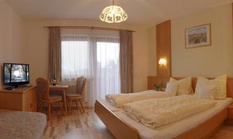 A cozy room with two beds, a television, and a small dining area. Large windows provide plenty of daylight and a pleasant atmosphere.
