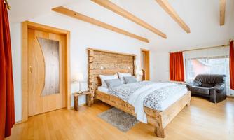 A modern bedroom with wooden details and a cozy bed. Large windows provide plenty of daylight and an inviting atmosphere.