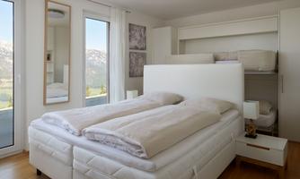 A modern bedroom with a double bed and a cozy atmosphere. Large windows offer a view of the mountains and plenty of natural light.
