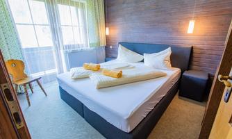 A bright and modern bedroom with a large double bed. There is a cozy chair and plenty of daylight coming through the windows.