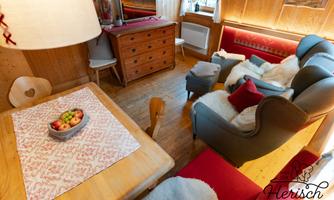 A cozy living room with wooden paneling, a dining group, and a television. The decor is friendly and inviting, perfect for relaxing evenings.