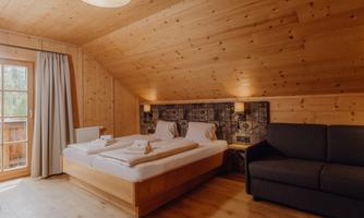A cozy bedroom with wooden paneling and a double bed. There is a seating area and a balcony with windows.