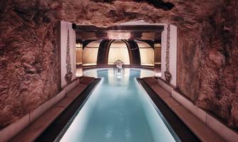 A luxurious indoor pool surrounded by natural stone walls. Soft lighting creates a relaxing atmosphere.