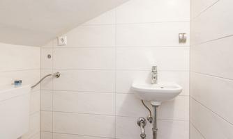 A small, bright bathroom with a sloping ceiling. There is a toilet, a sink, and modern white tiles.