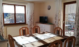 A bright living room with a dining table and chairs. Large windows bring in a lot of daylight and offer a view outside.