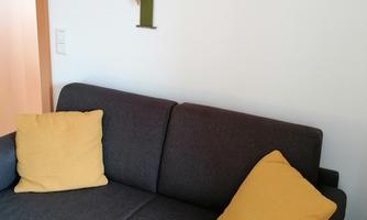 A cozy gray sofa with yellow cushions is positioned against a wall. Above the sofa hangs a picture frame with various photos.