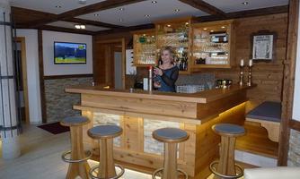 A cozy bar with wooden interiors and a bartender. In the background, glasses and a wall of televisions are visible.