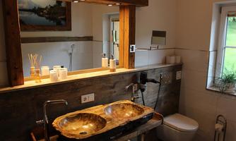 A modern bathroom with a wooden double sink and an elegant mirror. The walls are bright and there is a pleasant, natural atmosphere.